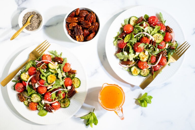 Horizontal overhead photo of two serving plates of Watermelon Arugula Salad on a white granite surface.
