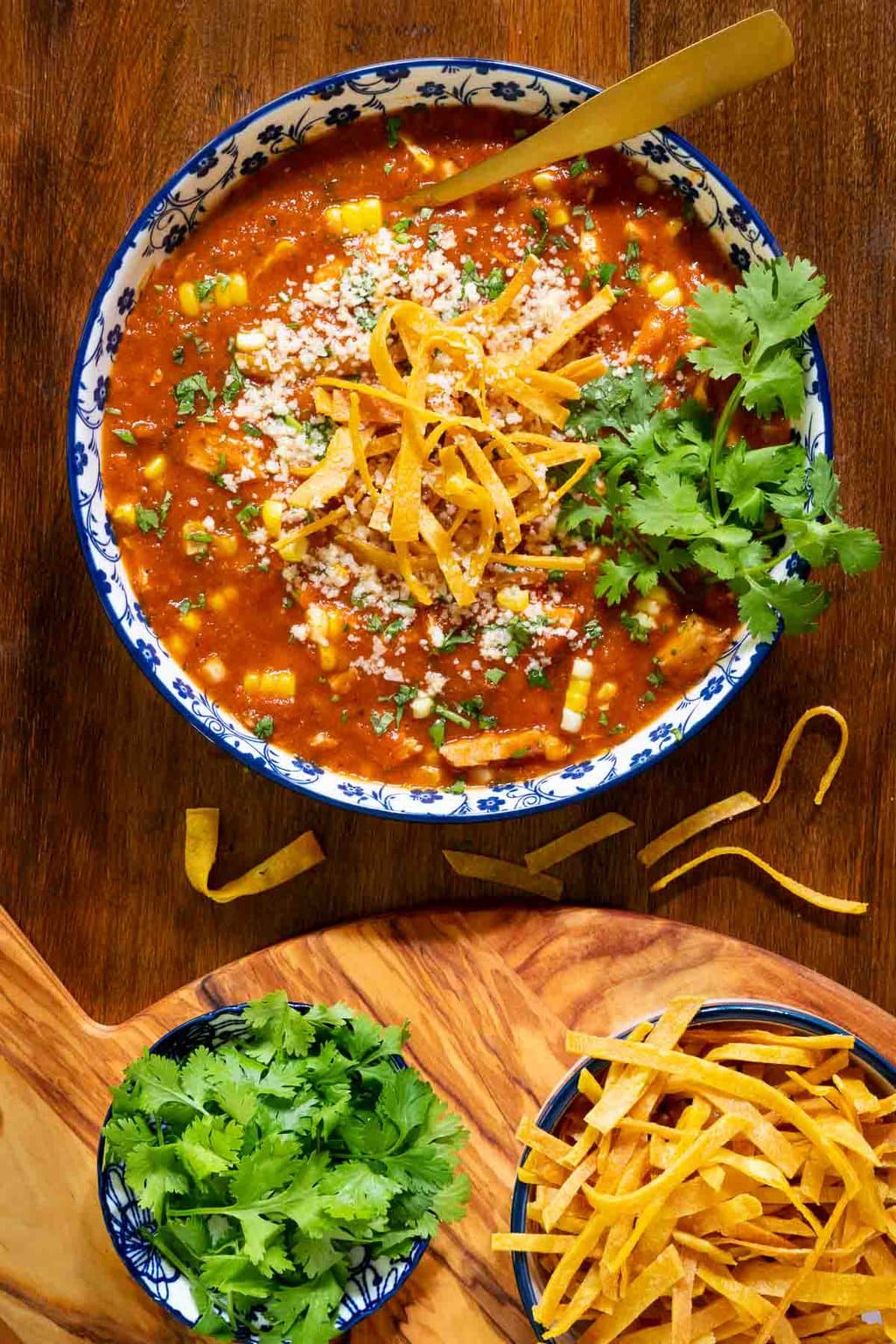 Vertical overhead photo of a bowl of Mexican Chicken Soup garnished with grated cheese, fried tortilla strips and fresh cilantro.