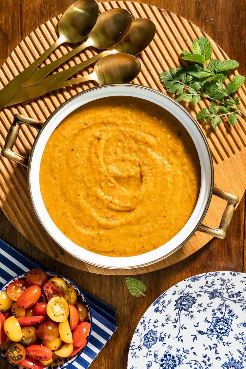 Vertical overhead photo of a pot of Butternut Red Lentil Dal with Gingered Tomatoes on a round wood plate