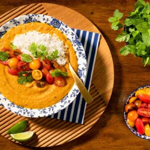 Horizontal overhead photo of a bowl of Butternut Red Lentil Dal with Gingered Tomatoes on a wood table.