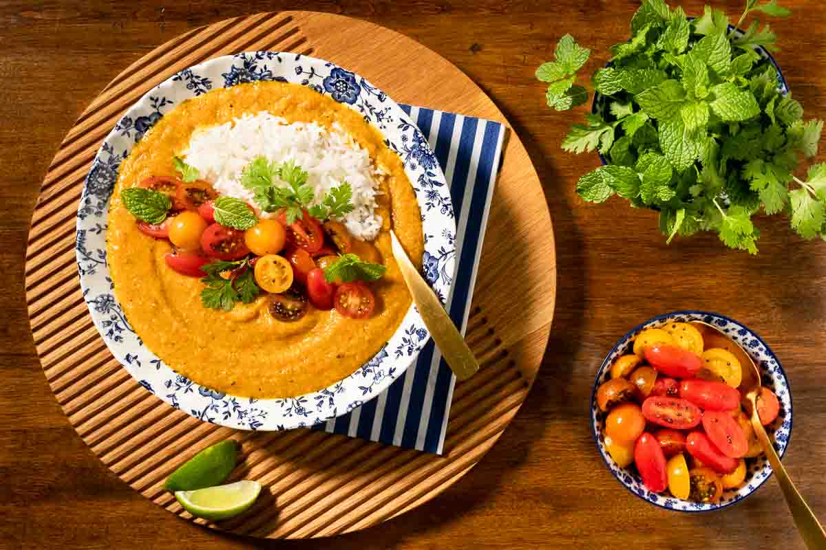 Overhead horizontal photo of a bowl of Butternut Red Lentil Dahl with Gingered Tomatoes on a round wood platter.