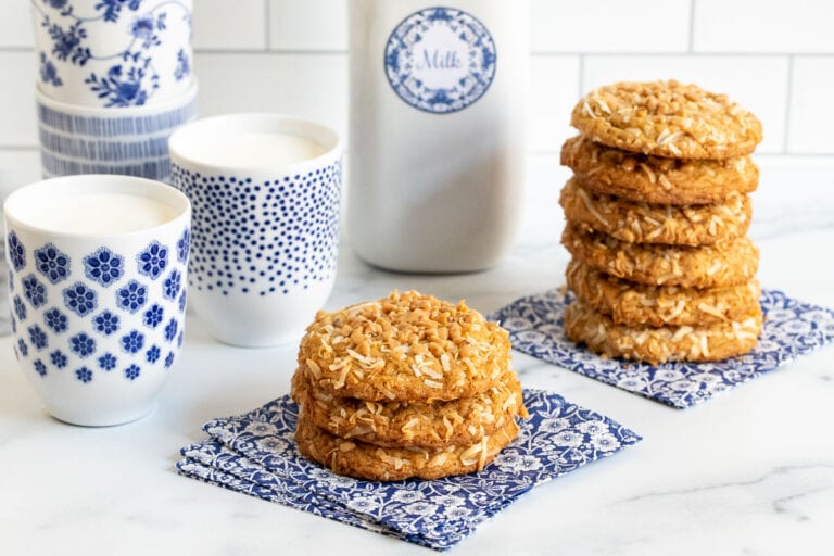 Vertical photo of stacks of Crispy, Chewy Carolina Coconut Cookies on blue and white patterned napkins.