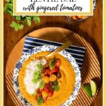 Vertical overhead photo of a bowl of Butternut Red Lentil Dal with Gingered Tomatoes on a round wood serving plate.