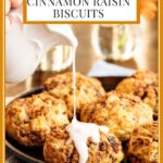 Vertical photo of a batch of Ridiculously Easy Cinnamon Raisin Biscuits with one of the biscuits being covered with vanilla icing.