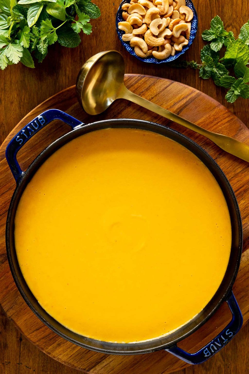Overhead vertical closeup photo of a blue cast iron pot of Roasted Coconut Butternut Squash Soup on a round wood platter.