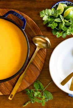 Horizontal overhead photo of a pot and serving bowl of Roasted Coconut Butternut Squash Soup on a wood table.