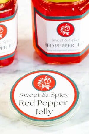 a custom label on a jar top with 2 jars of sweet and spicy red pepper jelly in the background