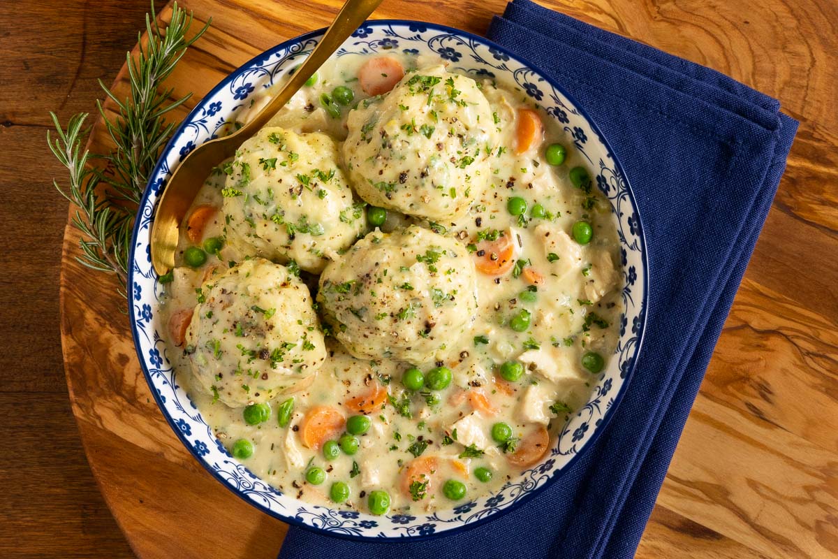 Horizontal overhead photo of a blue and white patterned serving bowl of Easy Chicken and Dumplings on a wood cutting board.