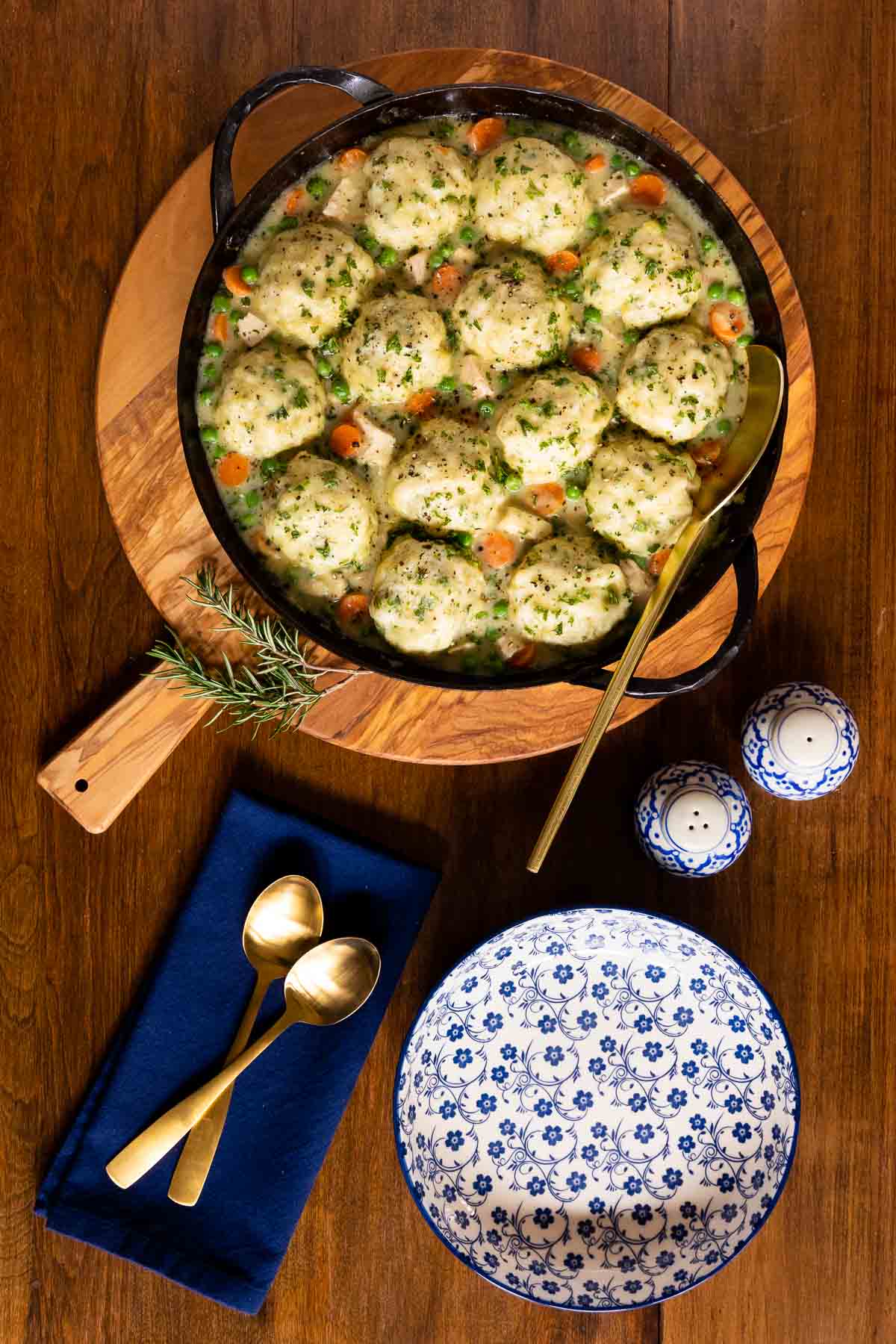 Vertical overhead photo of a cast iron pot filled with Easy Chicken and Dumplings on a wood serving board.