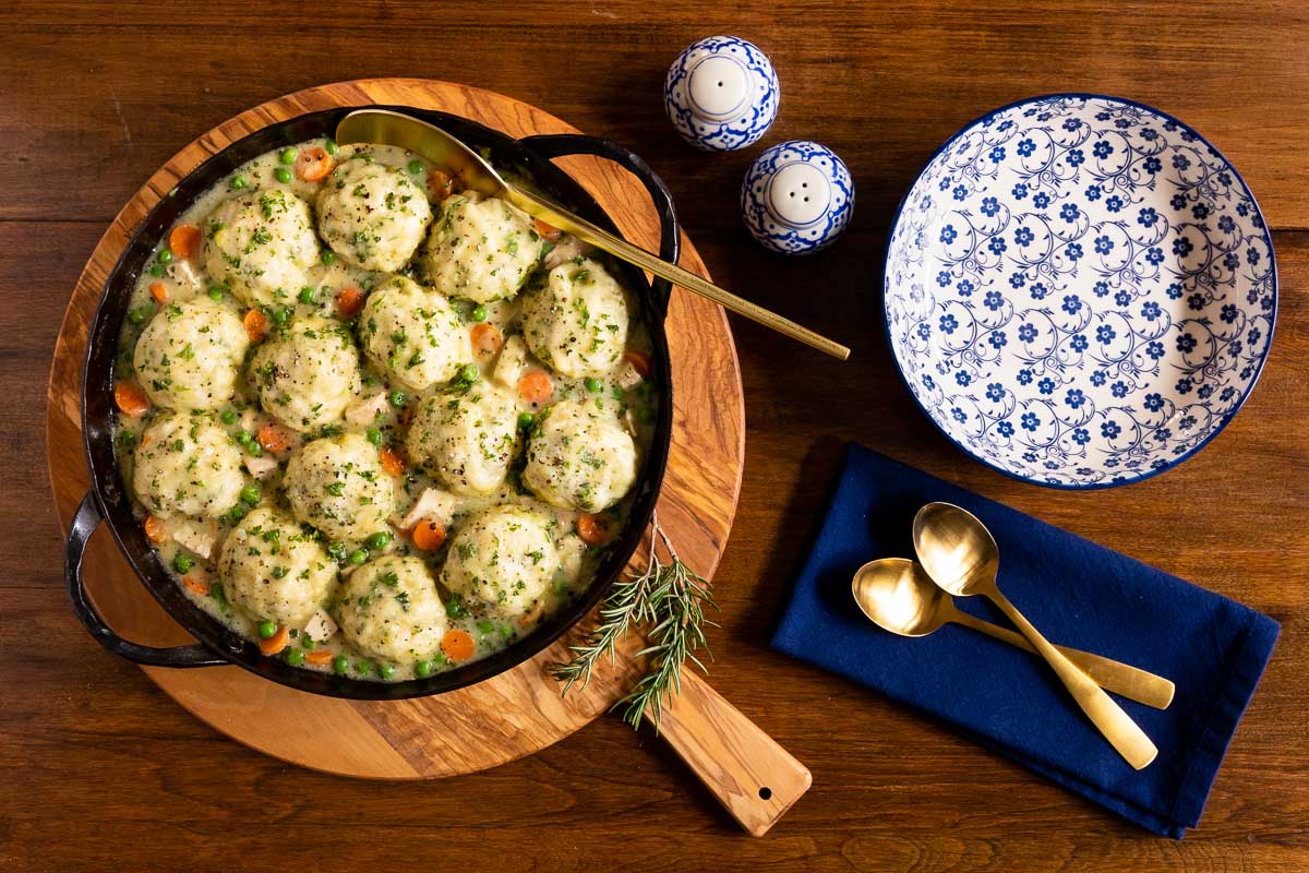 Horizontal overhead photo of a cast iron pot of Easy Chicken and Dumplings on a wood hot plate.