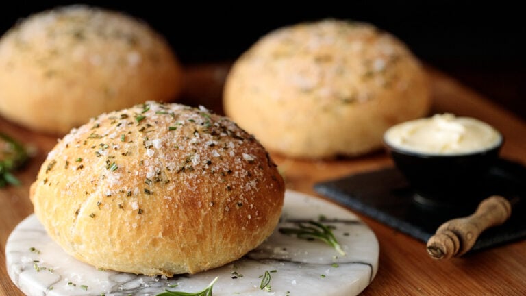 Horizontal closeup photo of a batch of Easy Rosemary Bread with butter on a wood table and marble plate.