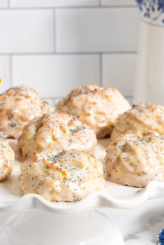 Horizontal photo of a batch of Lemon Poppy Seed Scones on a white scalloped pedestal serving plate.