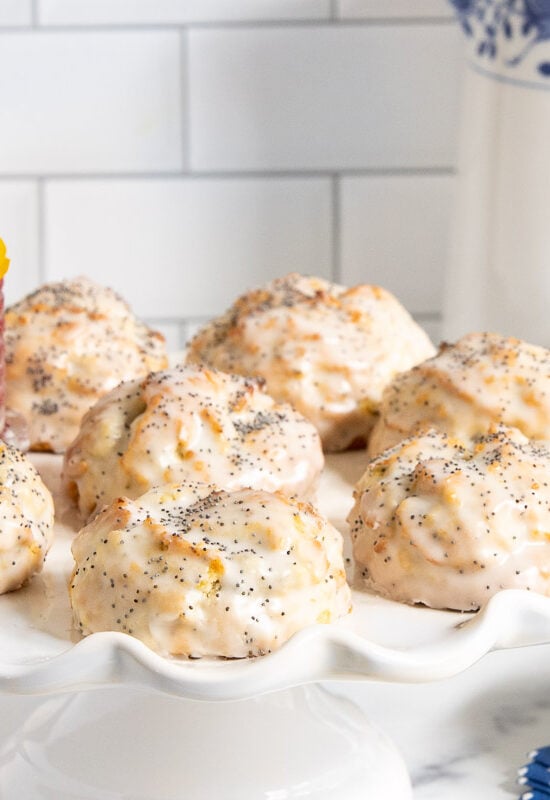 Horizontal photo of a batch of Lemon Poppy Seed Scones on a white scalloped pedestal serving plate.