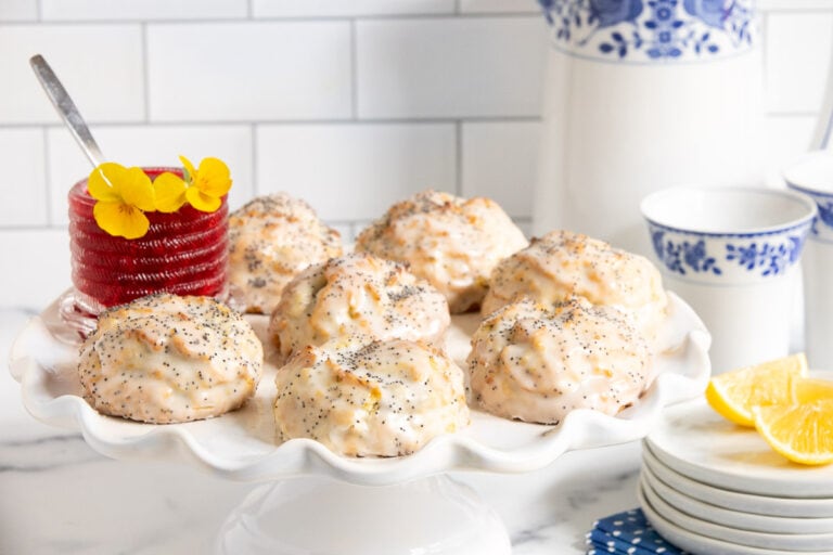 Horizontal photo of a batch of Lemon Poppy Seed Scones on a white scalloped pedestal serving plate.