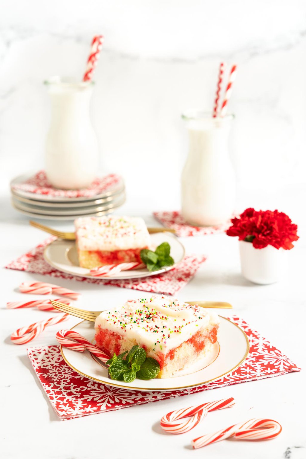Vertical photo of slices of Ridiculously Easy Candy Cane Sheet Cake on individual serving plates with jars of milk in the background.