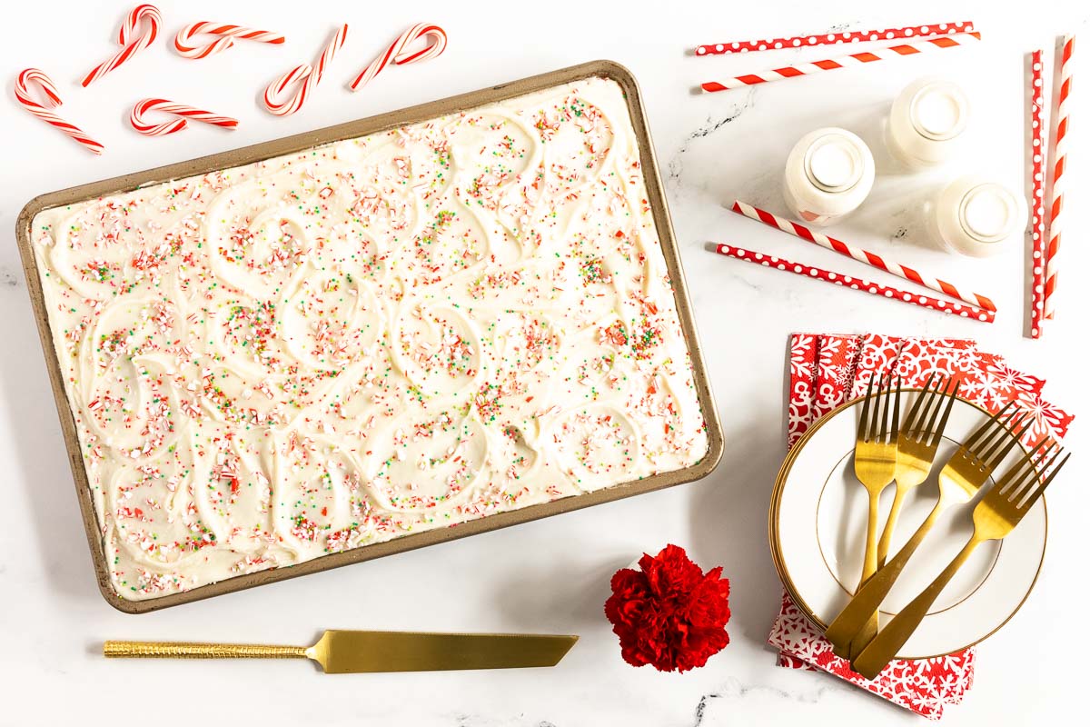 Horizontal overhead photo of a Ridiculously Easy Candy Cane Sheet Cake surrounded by candy canes, jars of milk and serving tools.