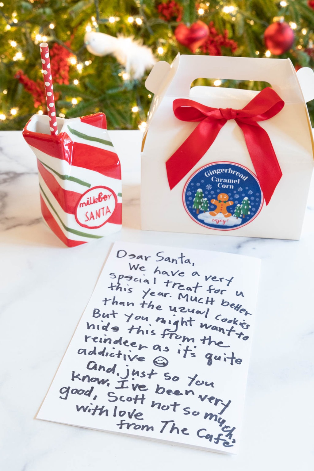 Vertical photo of a gift box of Ridiculously Easy Gingerbread Caramel Corn with a custom label and a letter to Santa from The Café.