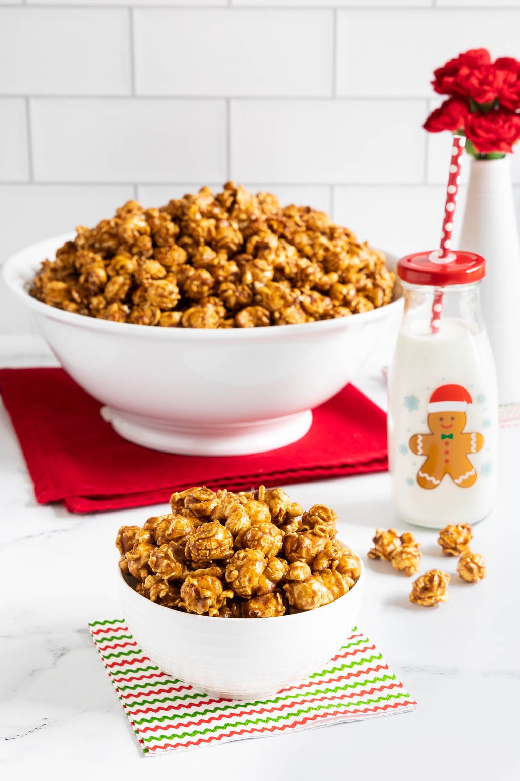 Vertical photo of bowls of Ridiculously Easy Gingerbread Caramel Corn on festive holiday napkins.