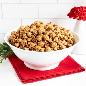 Horizontal photo of a large bowl of Ridiculously Easy Gingerbread Caramel Corn with a smaller serving bowl in the foreground.