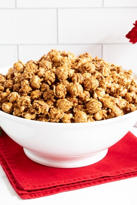 Horizontal photo of a large bowl of Ridiculously Easy Gingerbread Caramel Corn with a smaller serving bowl in the foreground.