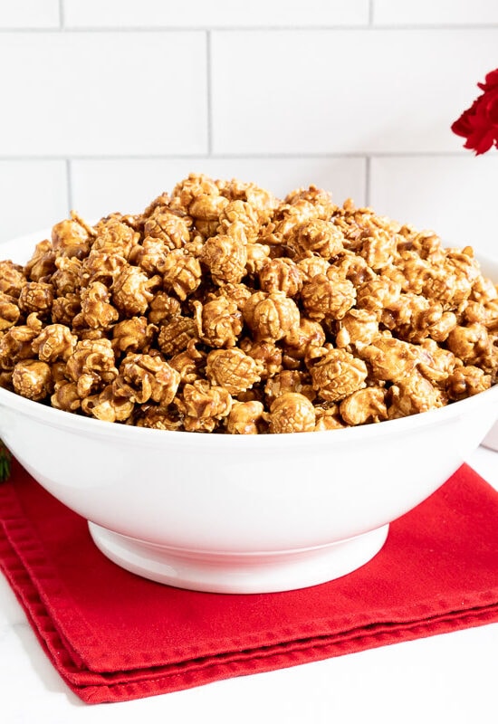 Horizontal photo of a large bowl of Ridiculously Easy Gingerbread Caramel Corn with a smaller serving bowl in the foreground.