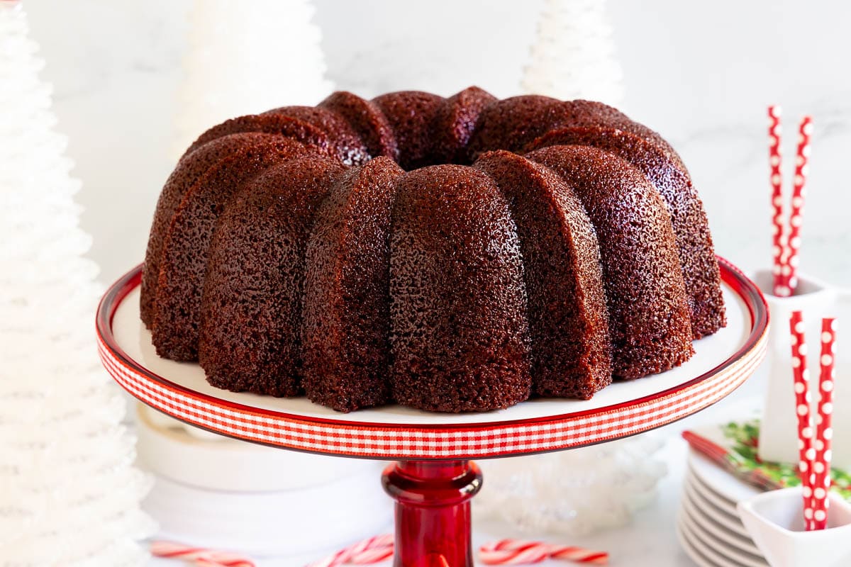 Horizontal photo of a Ridiculously Easy Peppermint-Glazed Red Velvet Bundt Cake on a red pedestal cake stand.