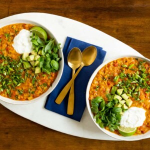 Horizontal overhead photo of two serving bowls of Curried Red Lentil Coconut Soup on an egg-shaped marble surface.