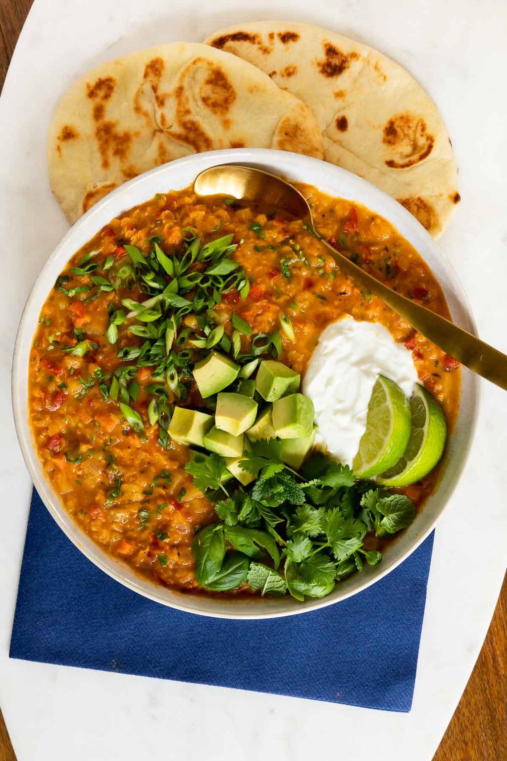 Vertical overhead photo of a serving bowl of Curried Red Lentil Coconut Soup with fresh baked naan bread on the side.
