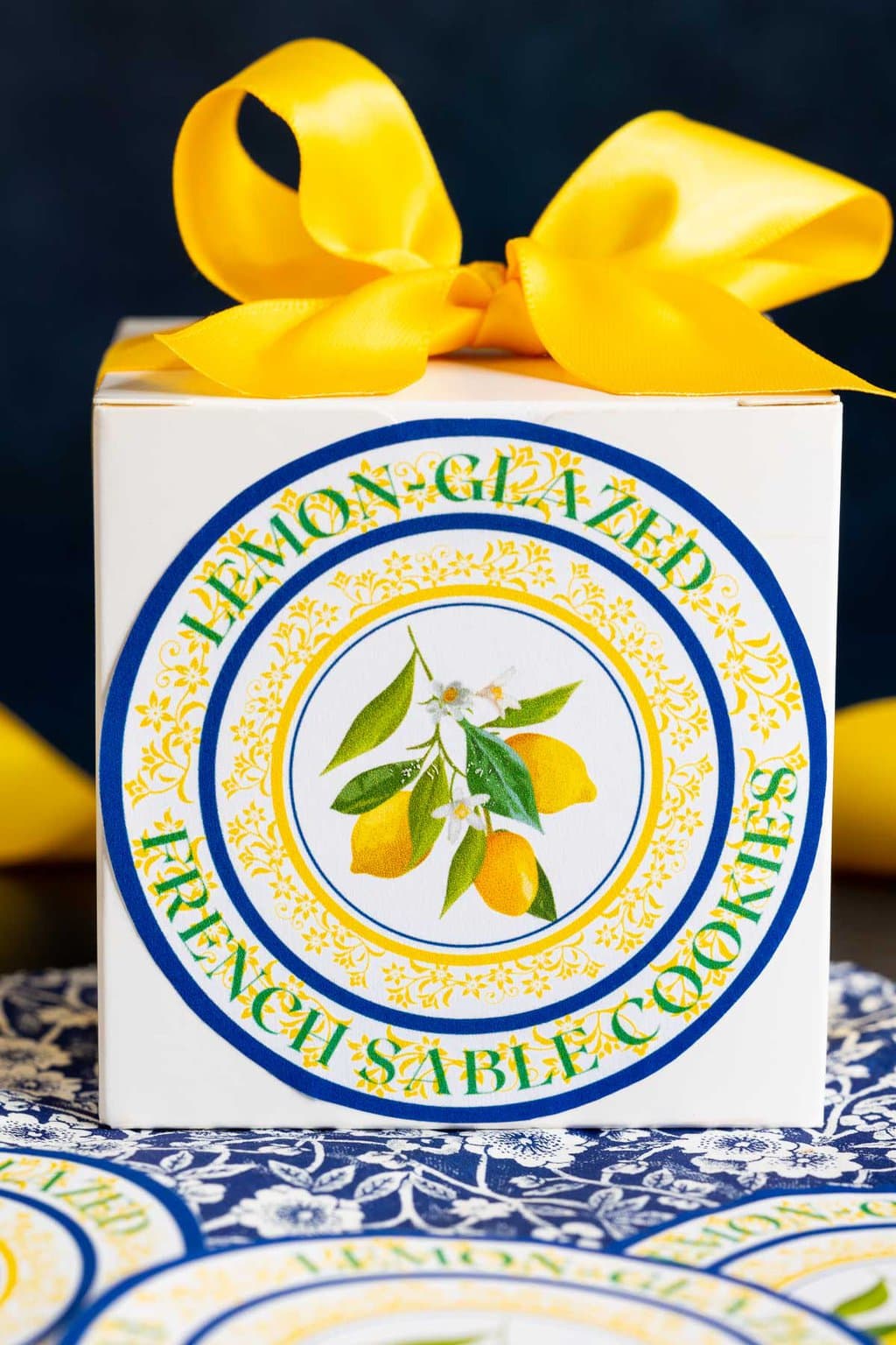 Vertical closeup photo of a custom Lemon-Glazed French Sable Cookie gifting label on a box with a yellow bow.