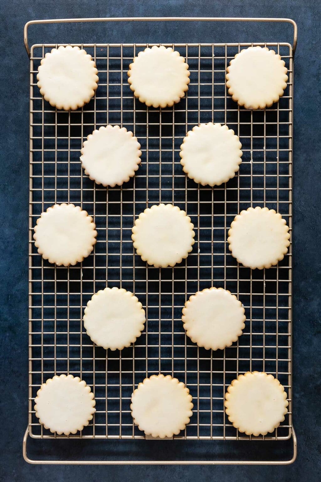Vertical overhead photo of a batch of Lemon-Glazed French Sable Cookies on a gold cooling rack.