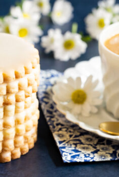 Horizontal photo of a stack of Lemon-Glazed French Sable Cookies next to a cup of coffee.