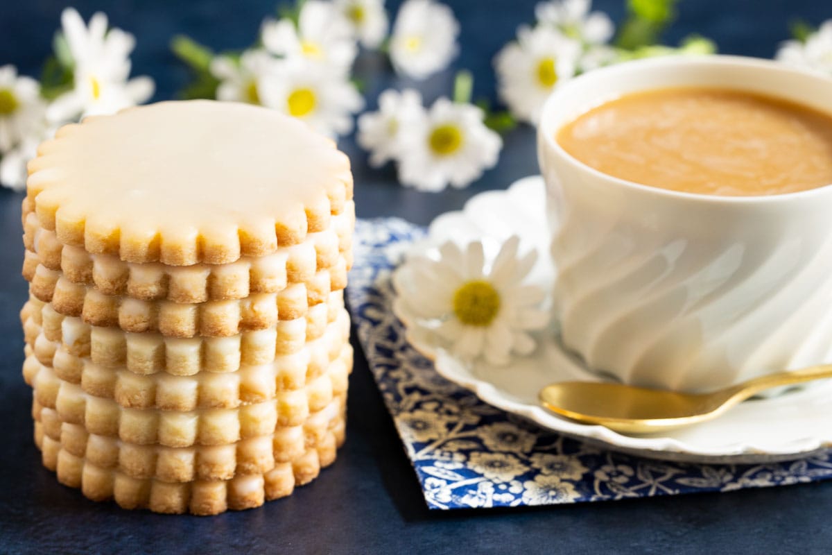 Horizontal closeup photo of a stack of Lemon-Glazed French Sable Cookies next to a cup of coffee.