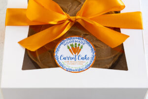 an easy carrot cake resting in a white box tied with an orange ribbon and a custom label affixed to the top