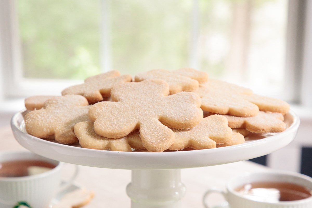 Horizontal closeup photo of a batch of Shamrock Irish Shortbread Cookies on a white pedestal serving plate.
