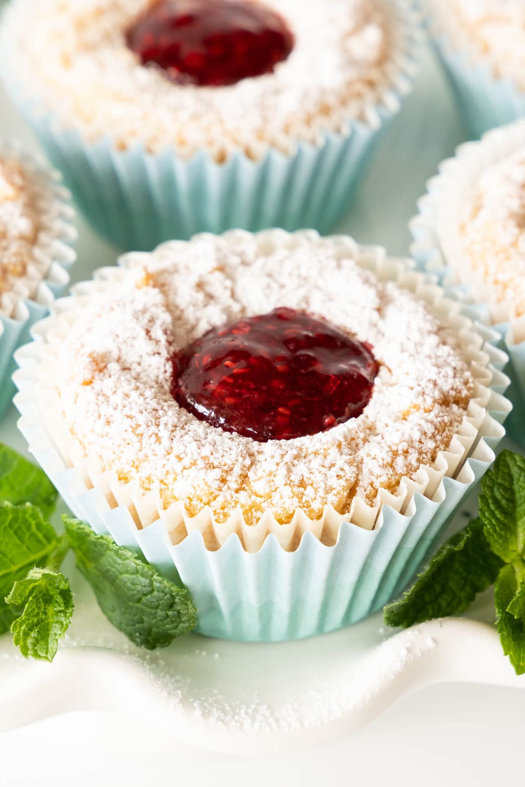 Vertical extreme closeup photo of Ridiculously Easy Scandinavian Raspberry Jam Tarts sprinkled with powdered sugar on a scalloped white serving plate.