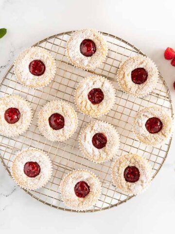 Horizontal overhead photo of a batch of Ridiculously Easy Scandinavian Raspberry Jam Tarts on a round gold cooling rack.