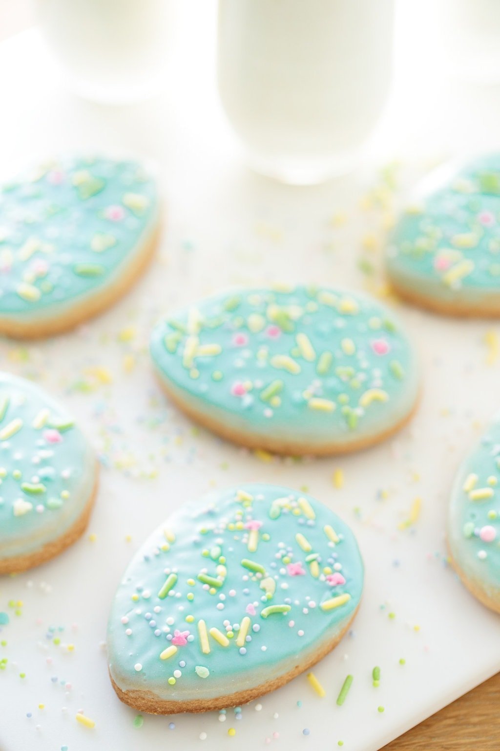 Vertical photo of a batch of Spring Shortbread Cookies with glasses of milk in the background.