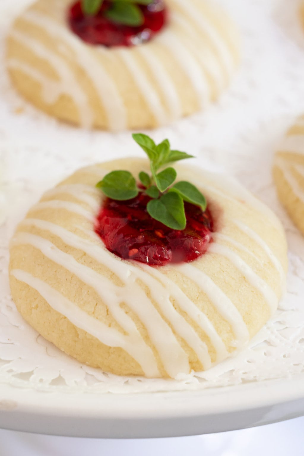 Vertical ultra closeup photo of a Almond Shortbread Thumbprints cookie with raspberry jam and a fresh herb garnish.