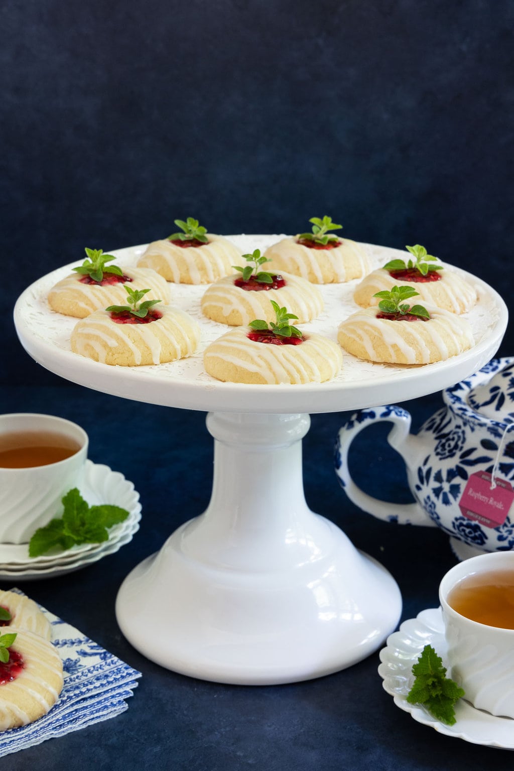 Vertical photo of a white pedestal serving plate filled with Almond Shortbread Thumbprints.