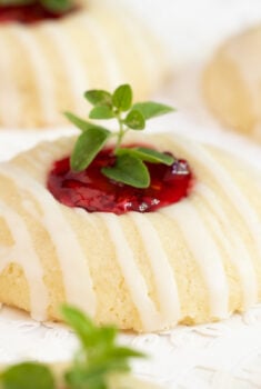 Horizontal photo of a batch of Almond Shortbread Cookies with raspberry filling and a fresh herb garnish.