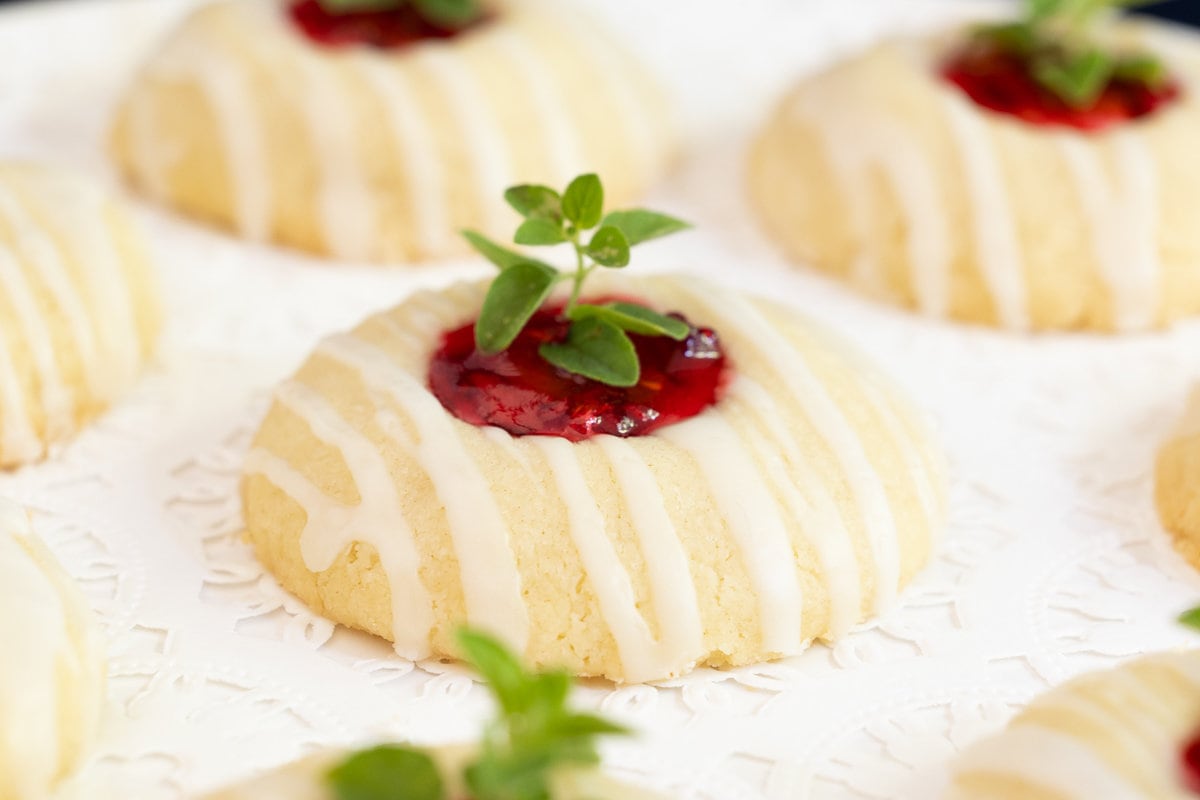 Horizontal photo of a batch of Almond Shortbread Cookies with raspberry filling and a fresh herb garnish.