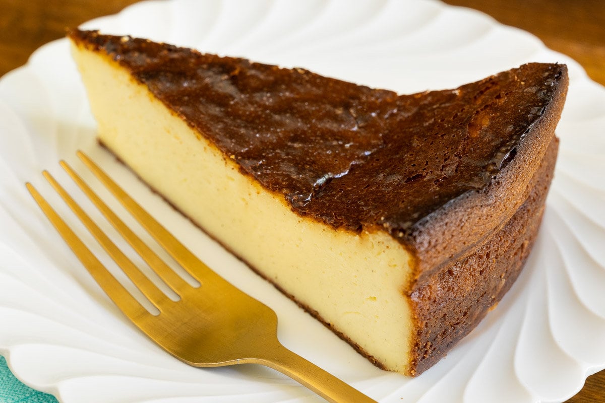 Horizontal closeup photo of a slice of Ridiculously Easy Basque Cheesecake (Tarta de Queso) on a white serving plate.
