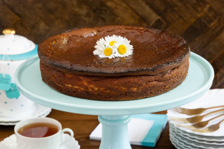 Horizontal photo of a Ridiculously Easy Basque Cheesecake (Tarta de Queso) on a turquoise pedestal serving plate.