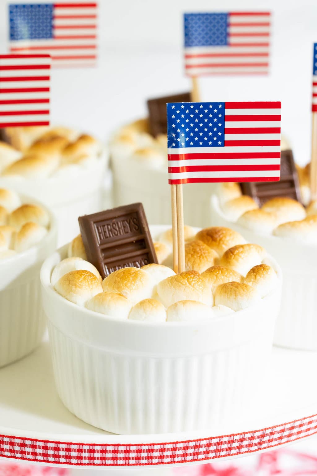 Vertical closeup photo of Easy Brownie S'Mores in Ramekins garnished with a Hershey's mini chocolate bar and an American flag.
