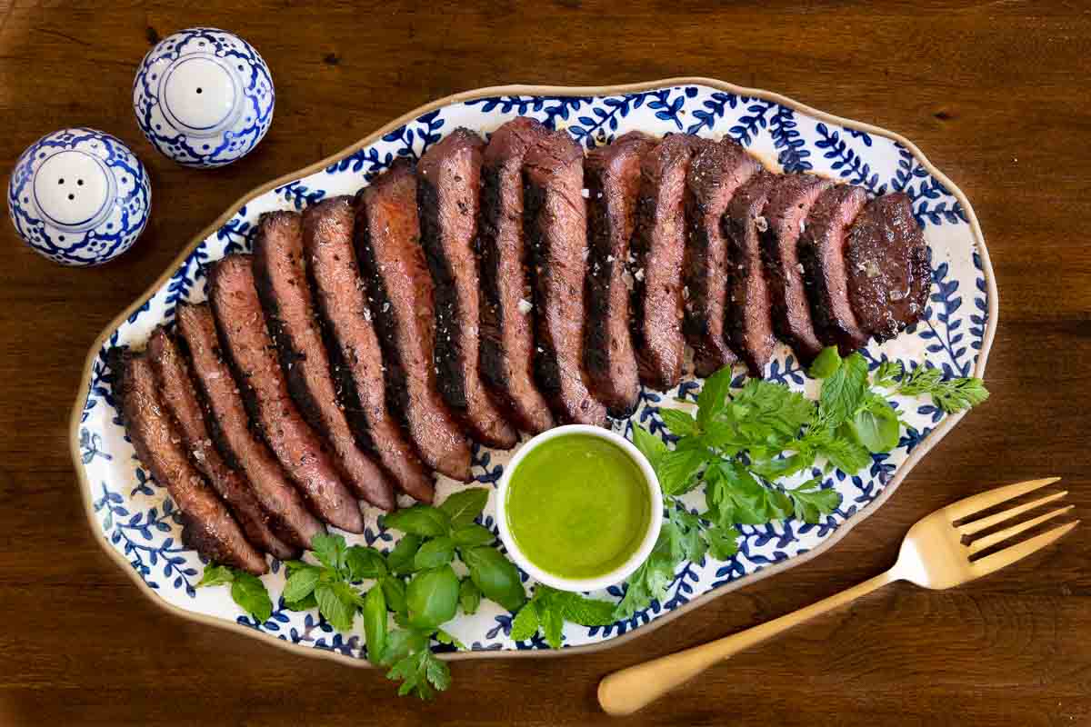 Horizontal overhead photo of a Vietnamese Grilled Flat Iron Steak on a blue and white patterned platter with Sweet Basil Vinaigrette.