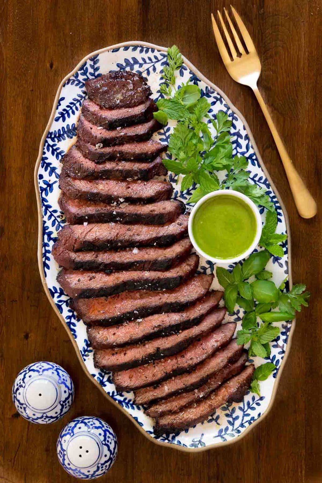 Vertical overhead photo of a platter of Grilled Vietnamese Flat Iron Steak with a cup of Sweet Basil Vinaigrette. 