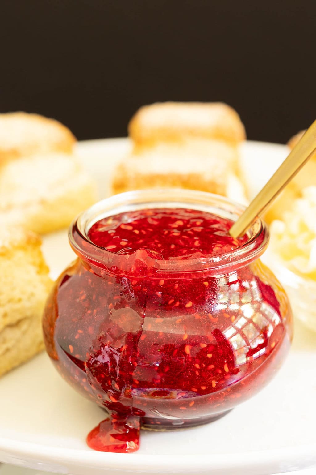 Vertical closeup photo of a Weck jar of Raspberry Freezer Jam surrounded by Ridiculously Easy Biscuits.