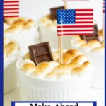 Vertical closeup photo of a batch of Make-Ahead Brownie S'Mores in Ramekins garnished with mini Hershey's chocolate bars and an American flag.
