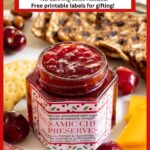 Vertical photo of a jar of Balsamic Sweet Cherry Preserves in the middle of a charcuterie board with a custom label for gift giving.