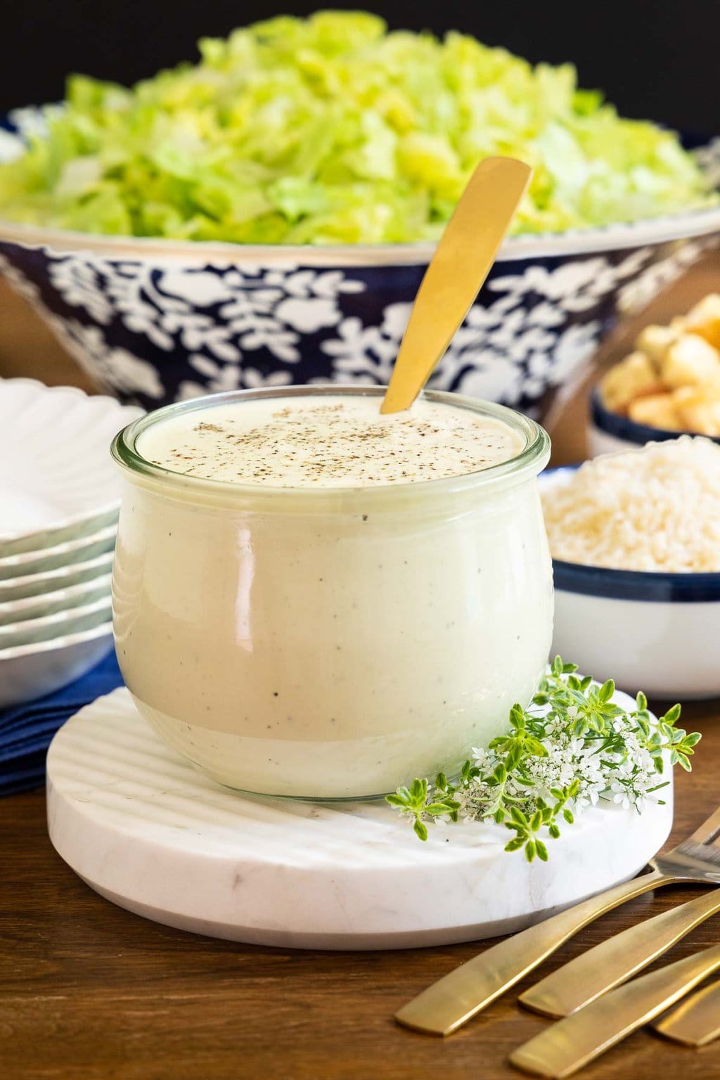Vertical closeup photo of a Weck jar of Ridiculously Easy Caesar Dressing with a caesar salad in the background.